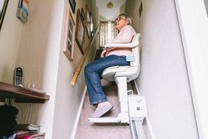 An image of an elderly woman seated in an automatic stair lift to move safely in her home.