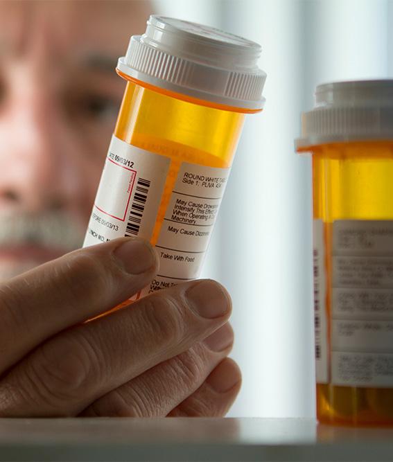 Inside a medicine cabinet looking out with a close-up of a man picking up a medicine bottle