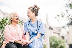 Senior woman sitting on a bench outside while holding hands with a home health care nurse