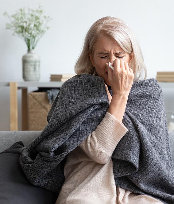 An elderly sick woman sneezing holding a napkin blow out a runny nose