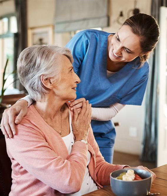 An elderly woman with a home healthcare nurse with breakfast at her home and a table in the living room.